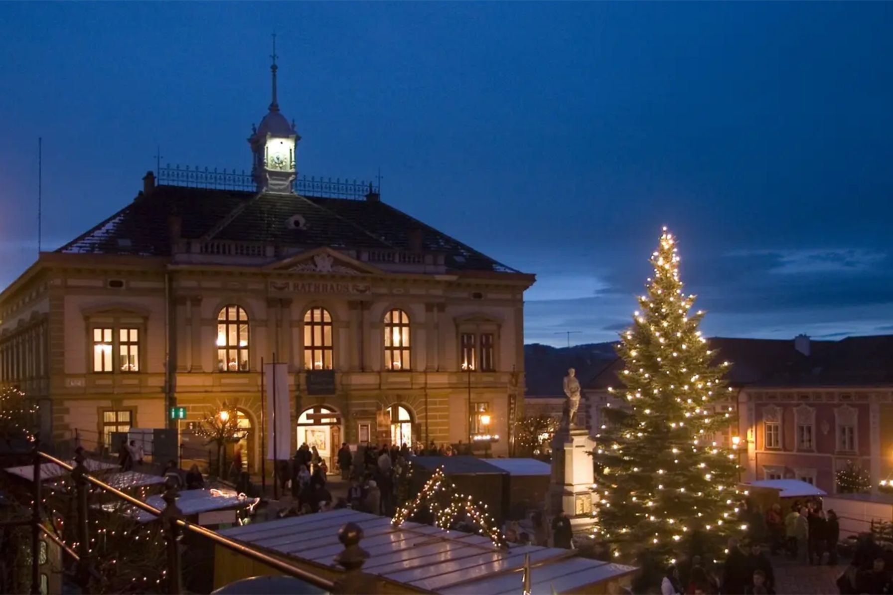 Weitraer Weihnachtsmarkt mit Ständen sowie beleuchtetem Baum und Rathaus im Abendlicht