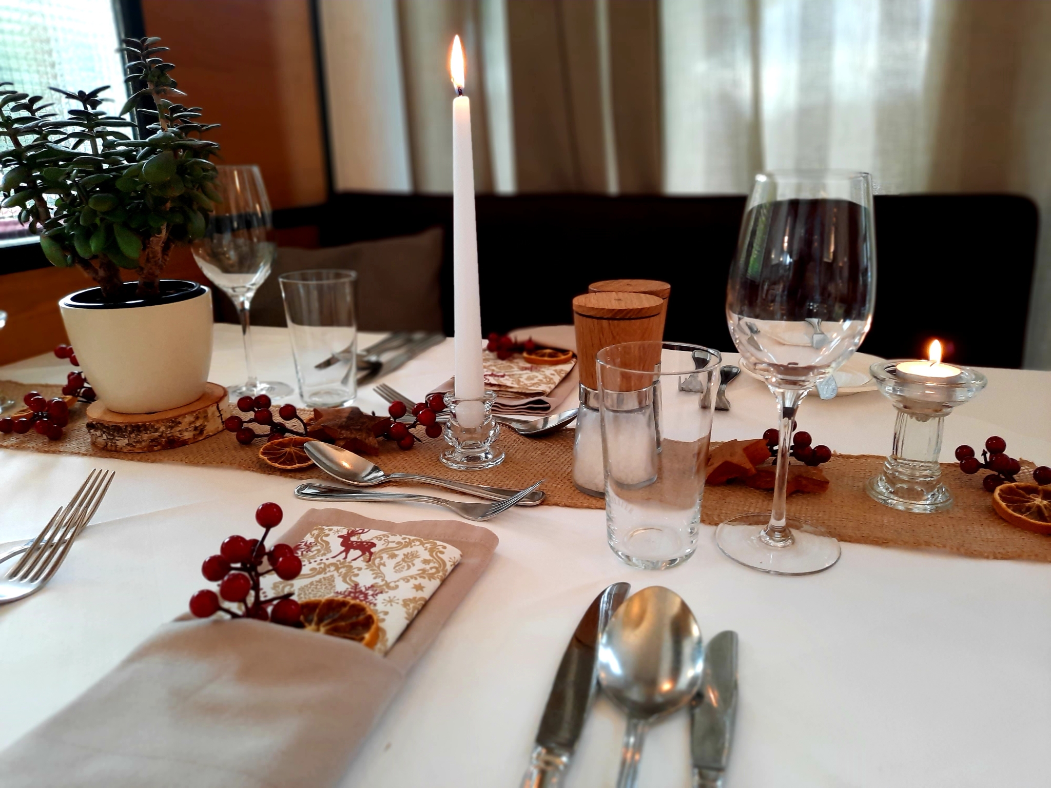 Ein elegant gedeckter Tisch mit Kerzen in Glasständern und Dekoelementen aus Holz und getrockneten Früchten
